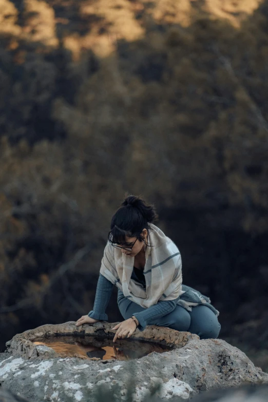 the woman sits on top of a rock and holds her head to her hands