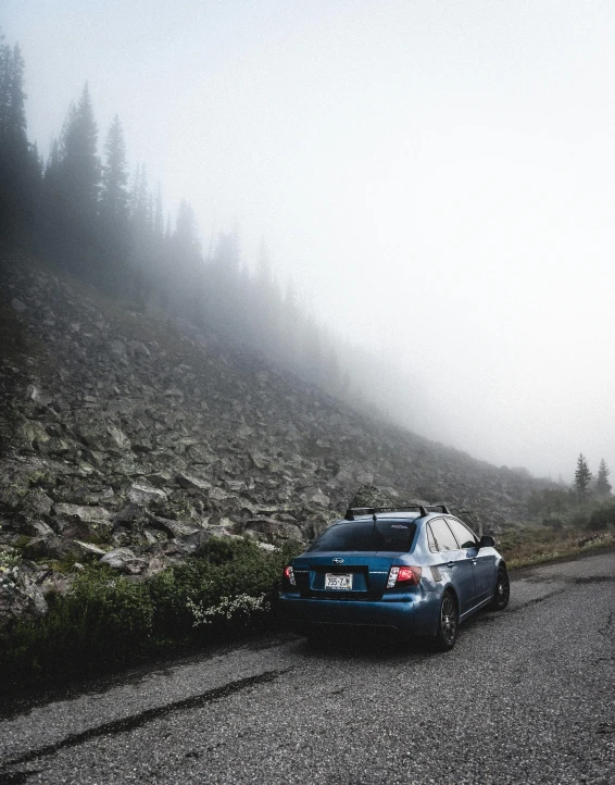 the blue car is driving down the road on the mountain