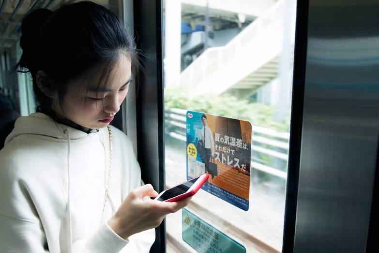 the young asian girl is holding her phone by the window