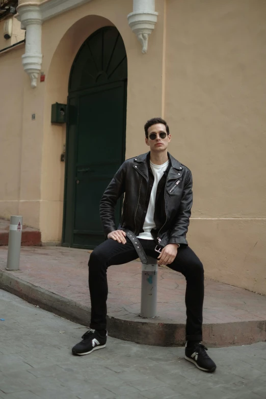 a man in a leather jacket sitting on the edge of a pole