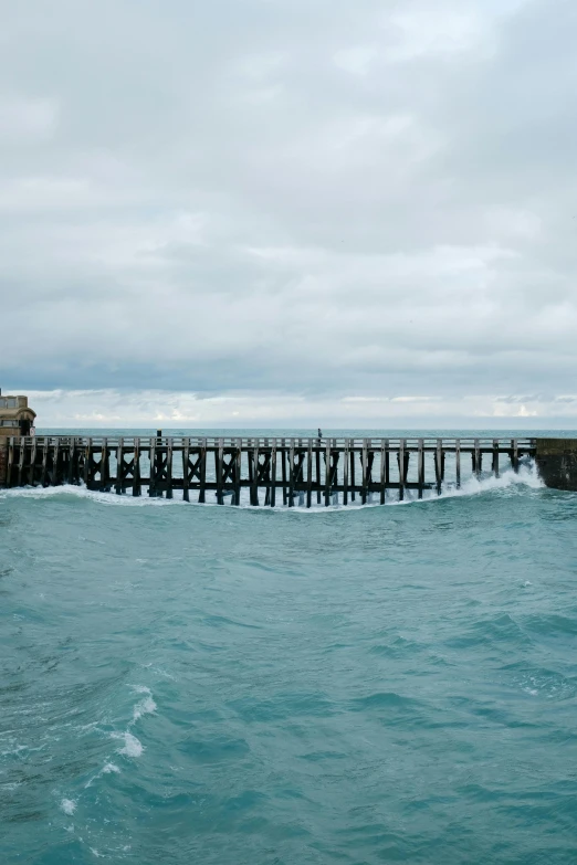 the ocean is choppy and blue, but it has a dock and light house near by