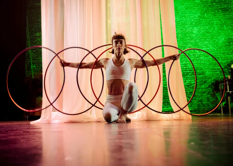 a woman kneeling down on the floor in front of a hoop with two hoop rings around her