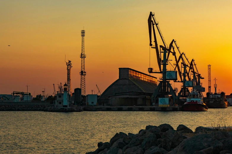 the sun rising behind cranes and ships in a harbor