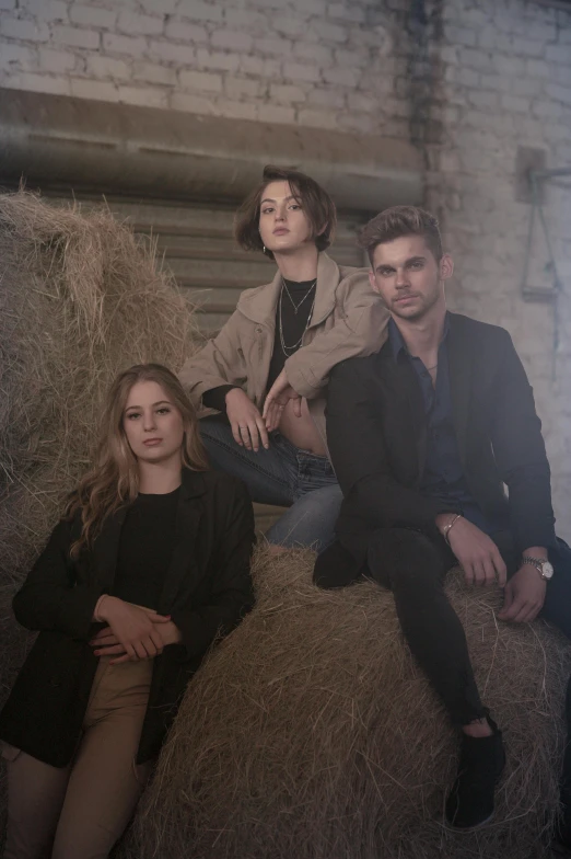 three people sitting on top of a bale of hay