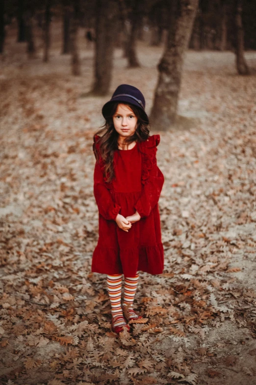  in red dress standing in leaves under a tree