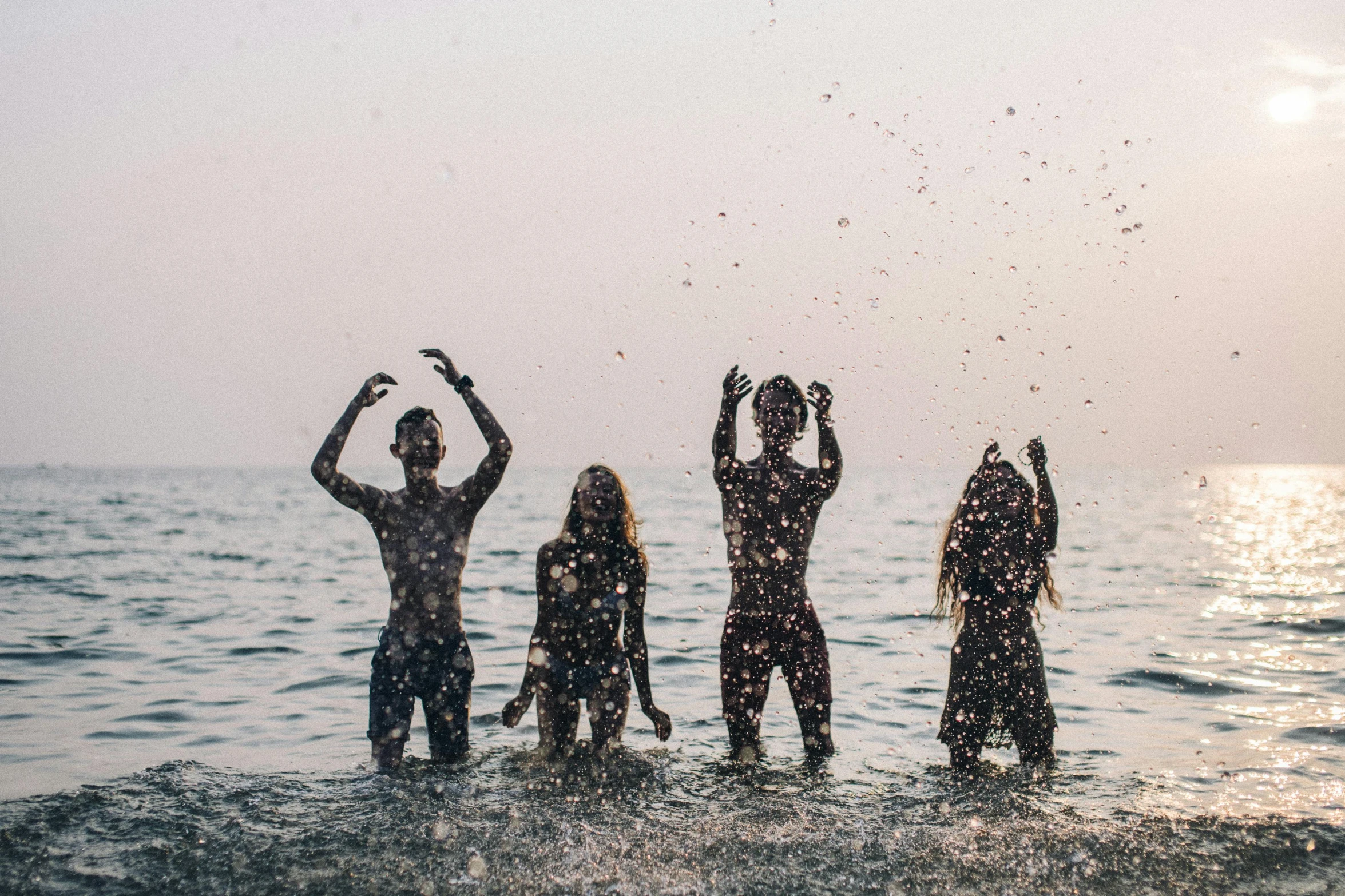 a group of three women in wet suits splashing in water with their hands