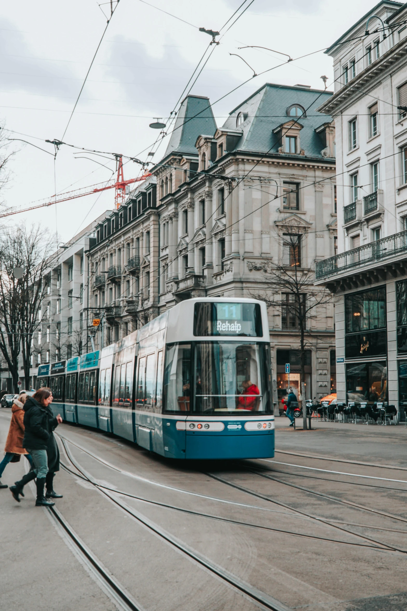 a blue and white electric tram moving past two people