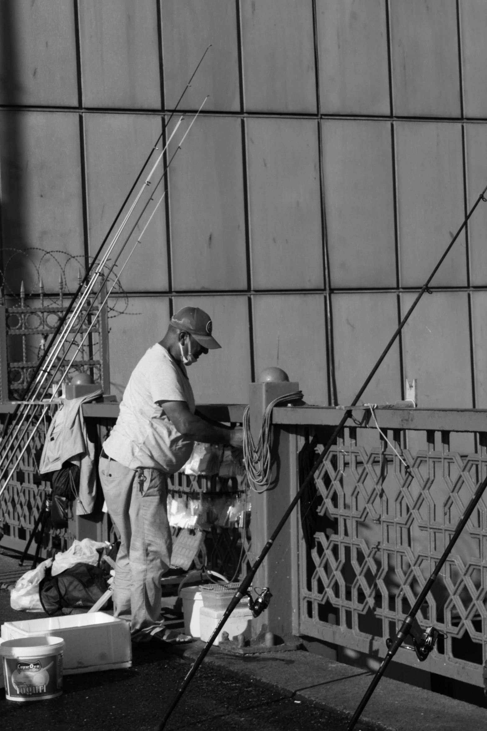 black and white pograph of man sitting on dock with fishing rods