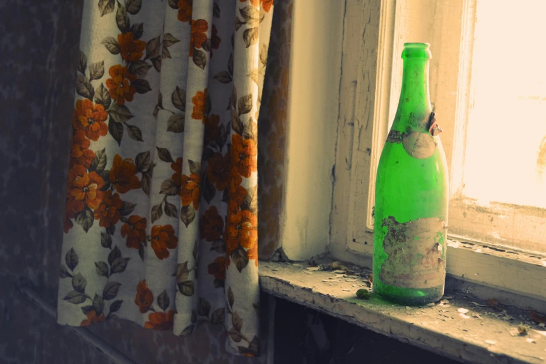 an empty green bottle on a windowsill next to curtains