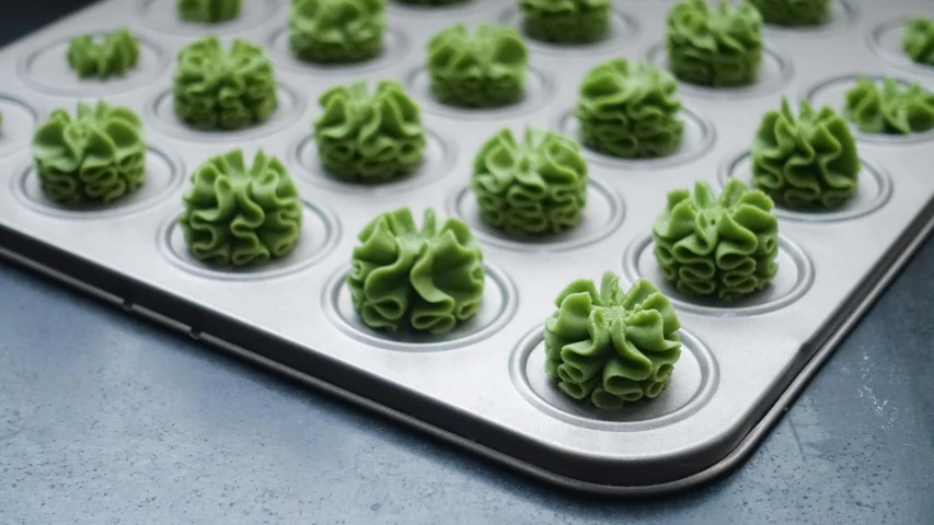 a muffin tray filled with green cupcakes with curls