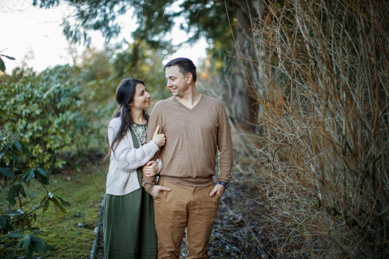 a man standing next to a woman near bushes