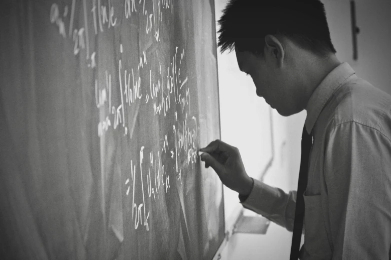 a man in shirt and tie writing on a blackboard