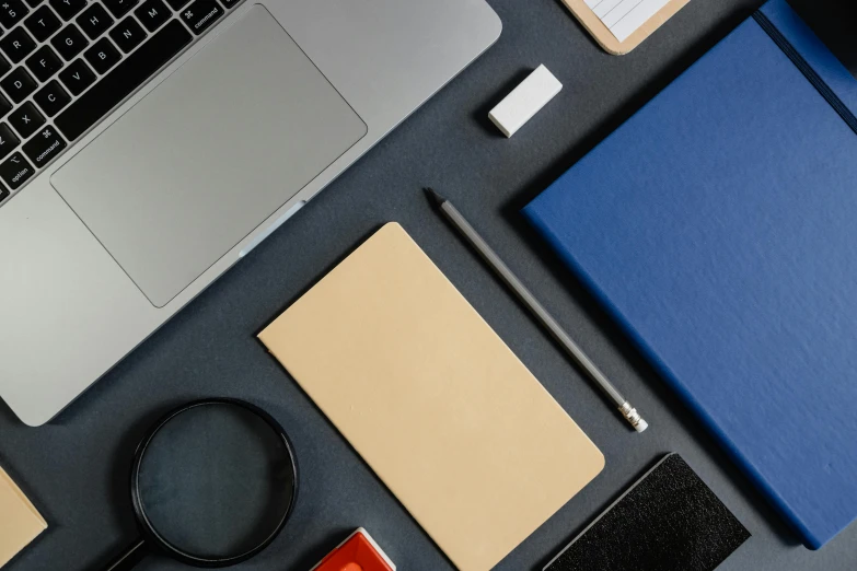 some notebooks and pens next to a laptop