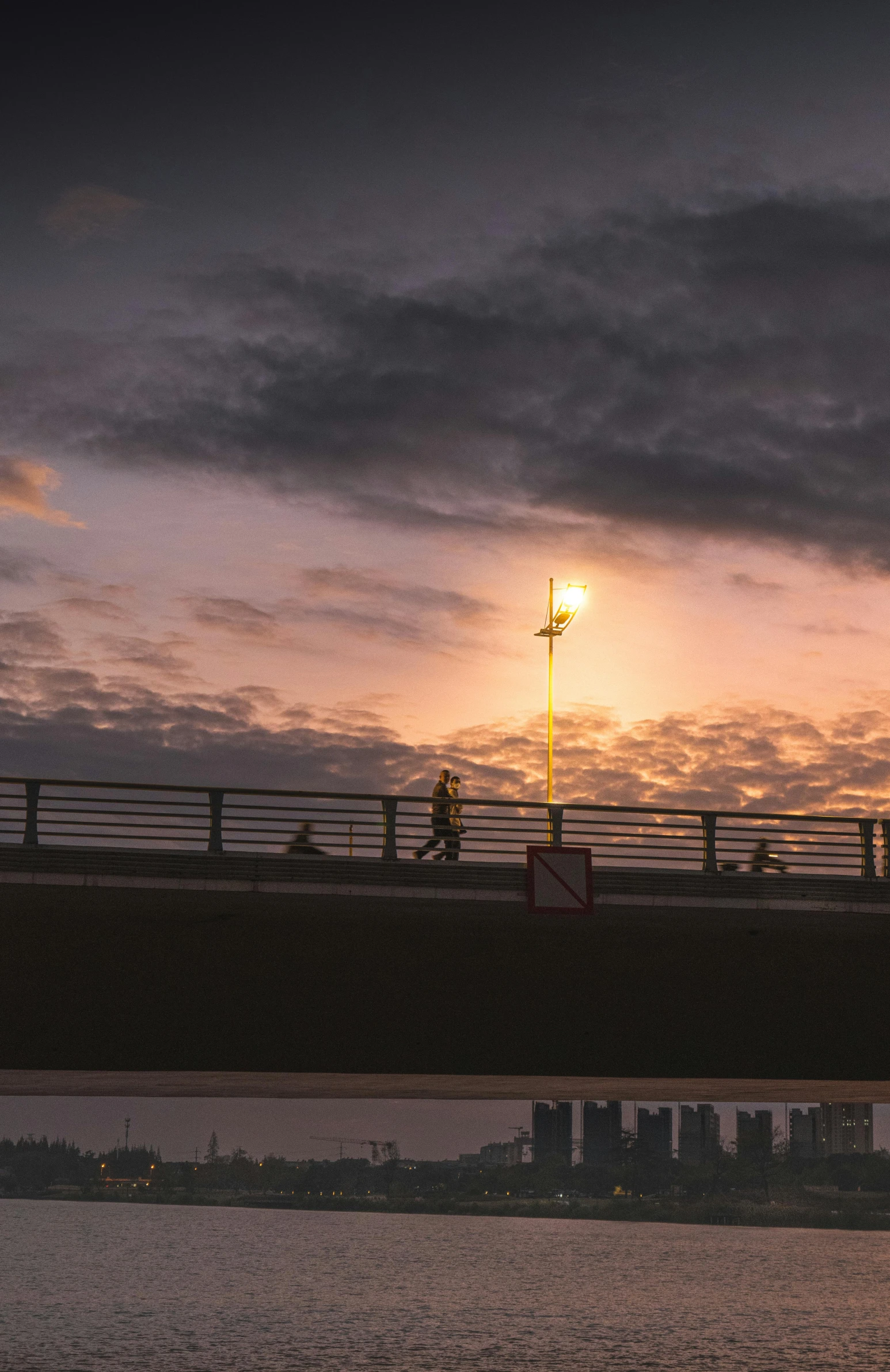 a bridge and street lights at sunset, as seen from the water