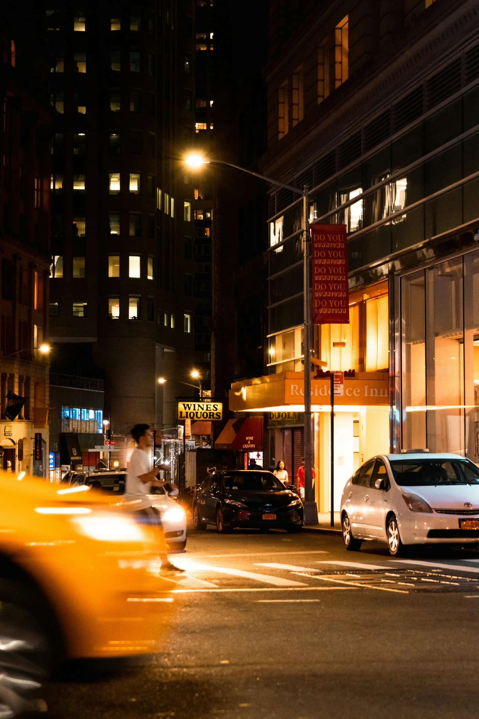 cars move by in front of an illuminated store at night