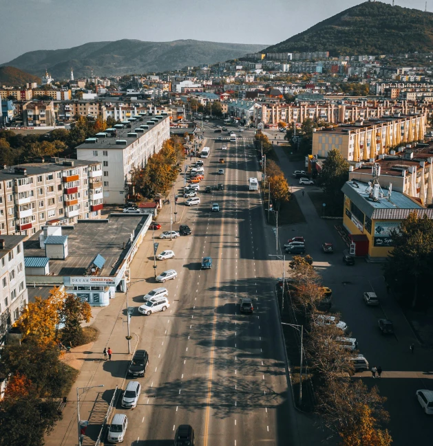 city buildings sit on either side of the street as cars drive down it