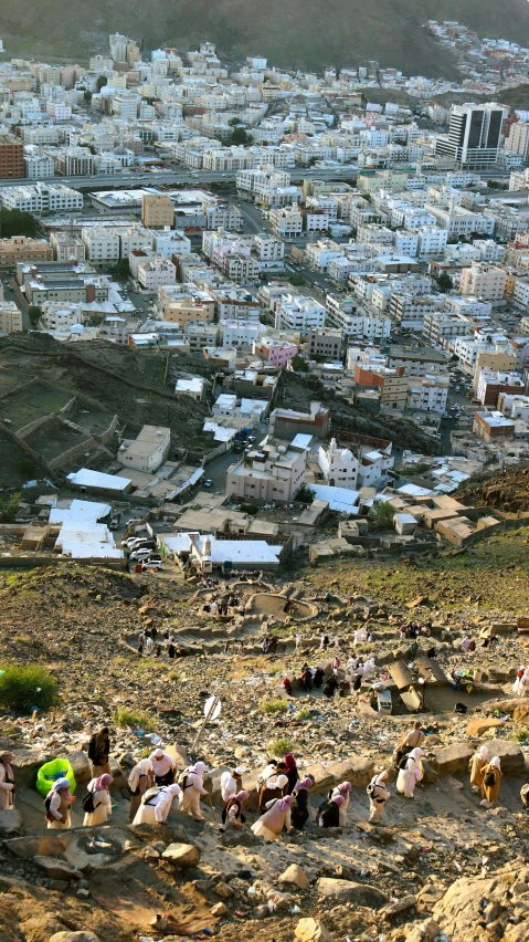 several people walking up a dirt hill next to a city