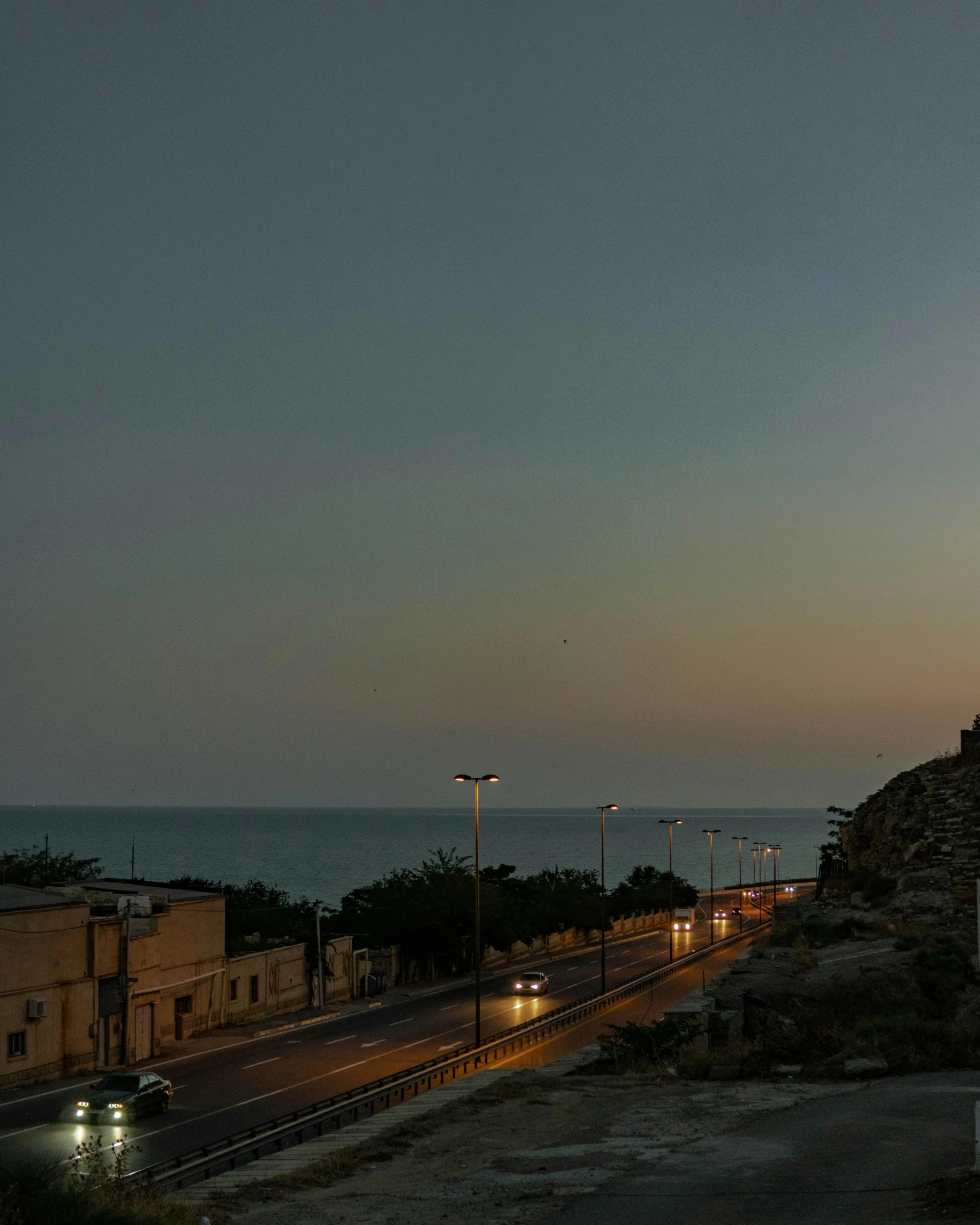 a night time s of a lighthouse on the coast with cars driving by