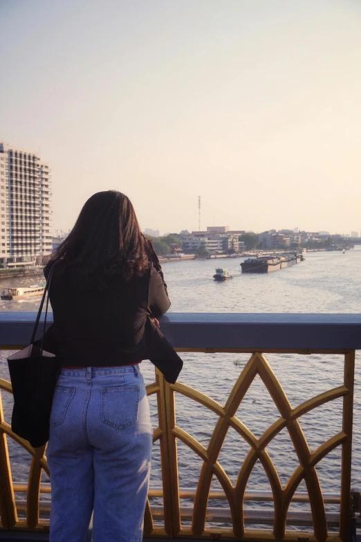 the woman is standing near a fence looking at the water