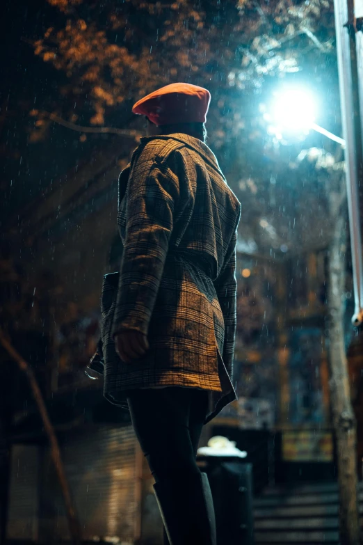 man in coat at night wearing umbrella and red hat