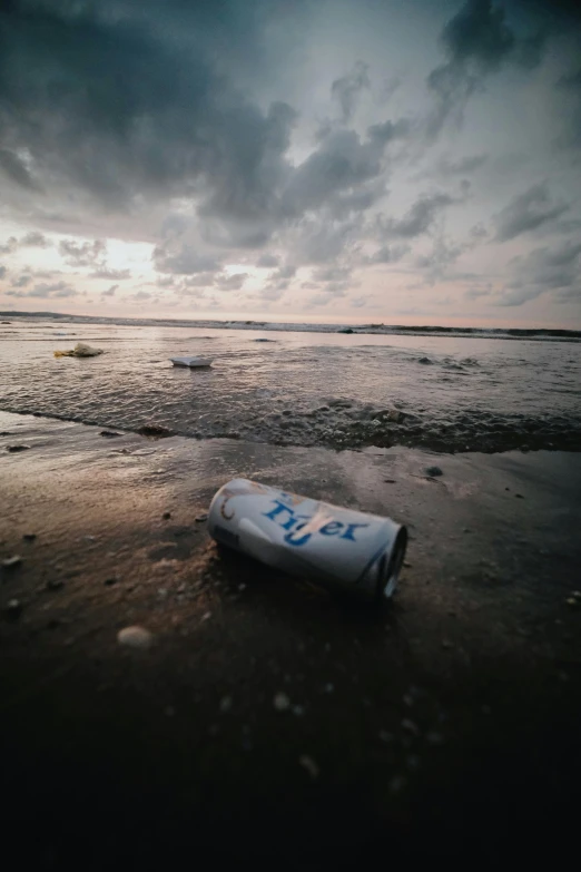 an empty soda bottle sitting on the beach under a cloudy sky