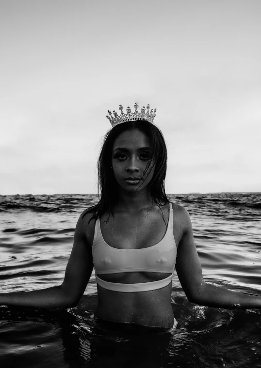 a woman standing in the water wearing a crown