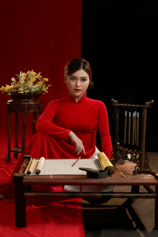 a woman wearing a red dress, with her hand in a tray with cake, next to a wooden chair and red curtain