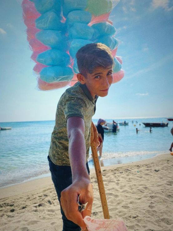 a boy holds a large blue and pink umbrella on a beach