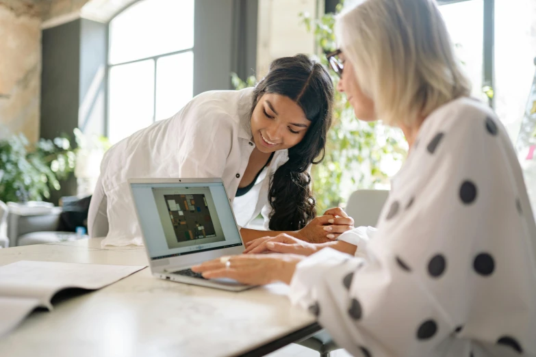 two woman on their laptops smiling at one another