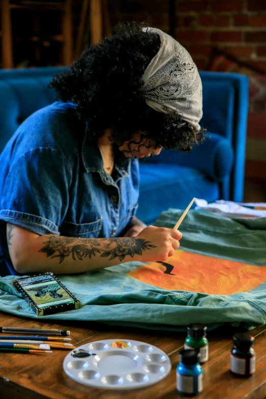 tattooed man painting on canvas at table with art supplies