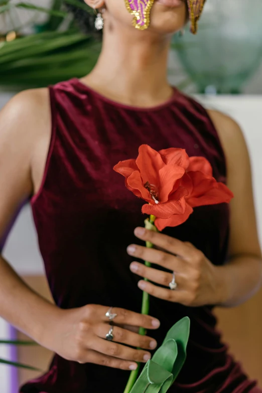 a woman holds a small red flower near her nose