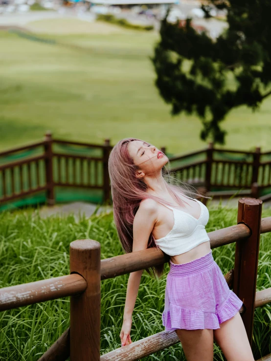 a woman with pink hair is leaning on a wooden fence