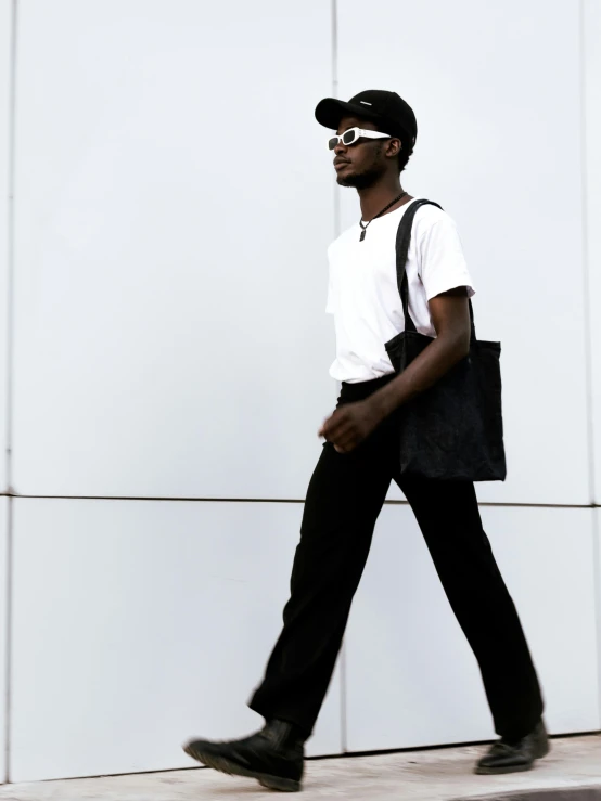 a man walking down the sidewalk wearing sunglasses and holding a black bag