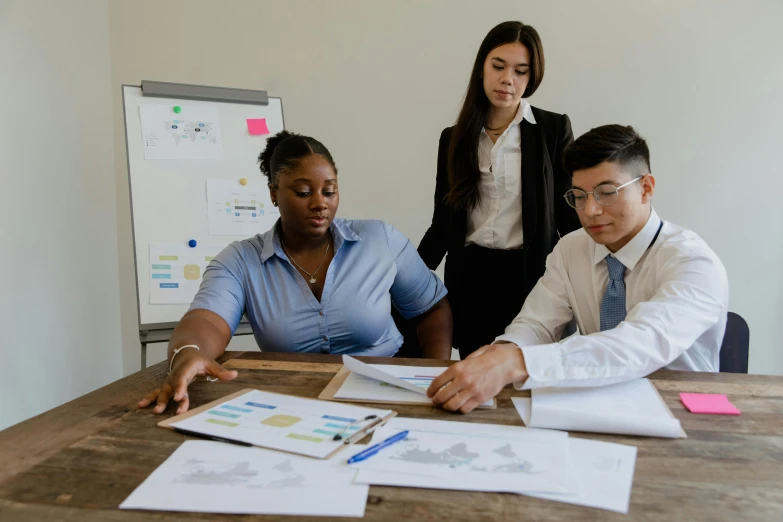 three people looking at papers on a wooden desk