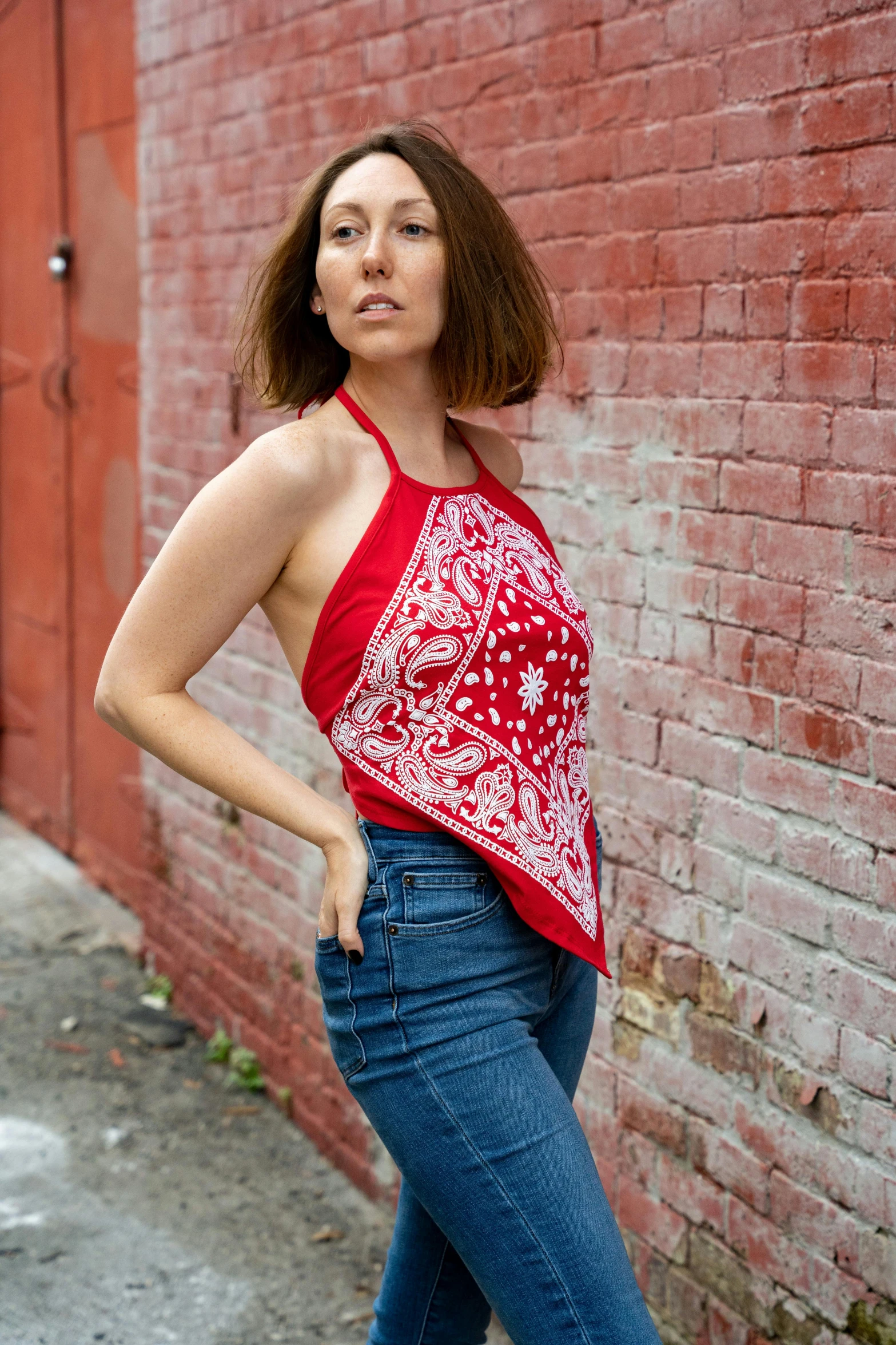 a woman poses in a red top by the brick wall