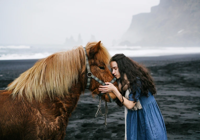 a woman pets a pony with the bridle on her face