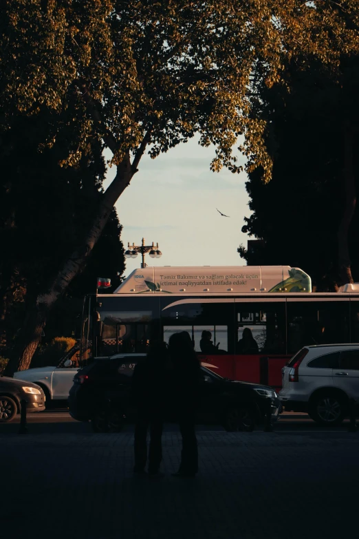 a couple standing in the shadow next to a red and white bus