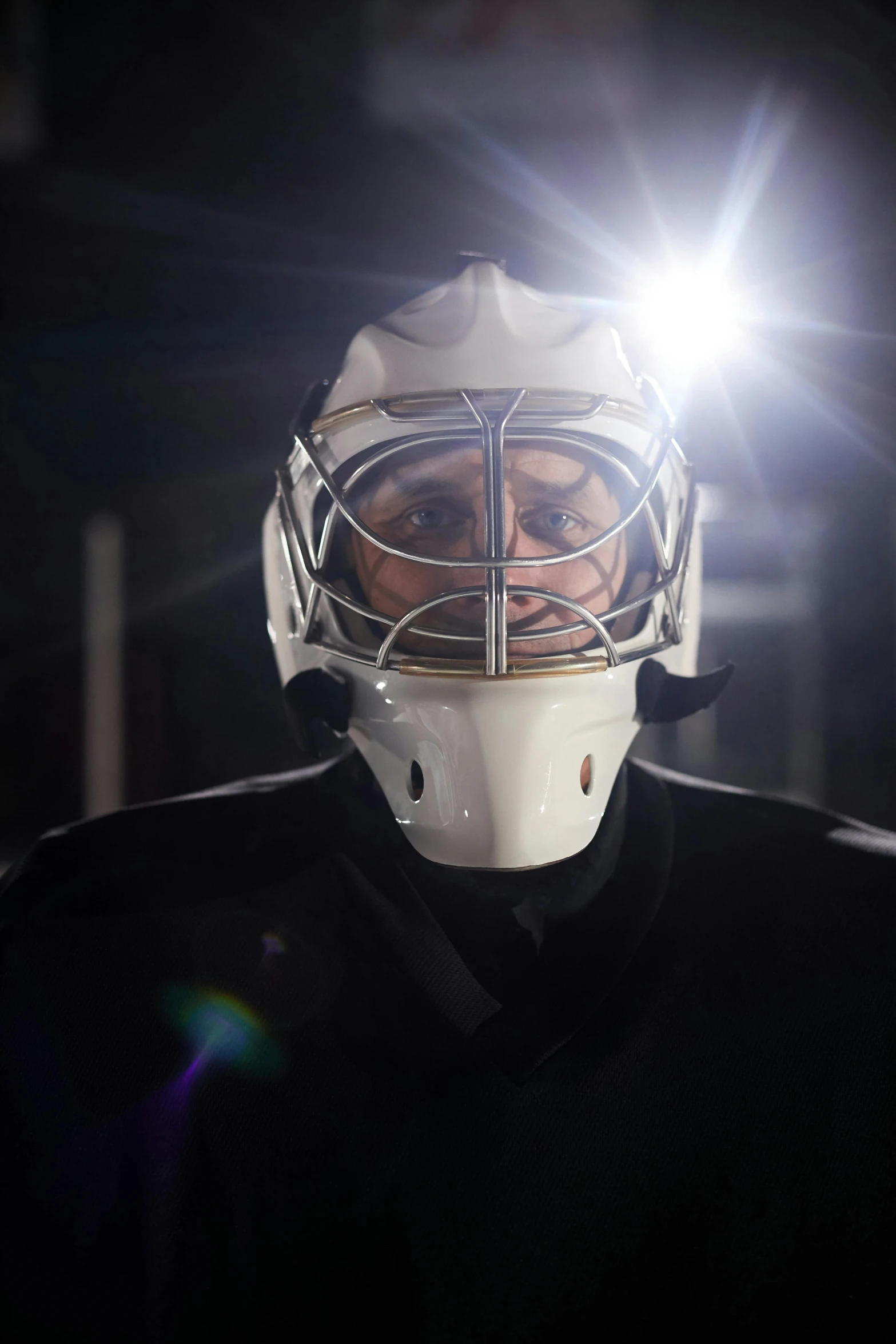 hockey goalie with helmet lit by the spotlight