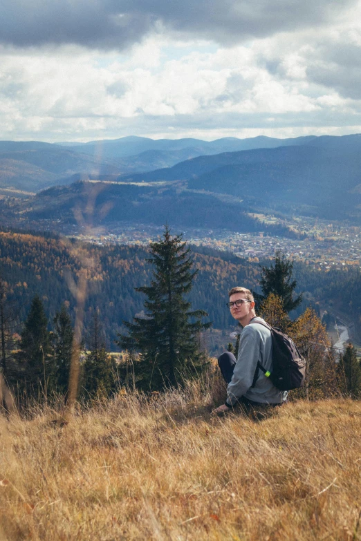 a man sits on a hill on a cloudy day with a backpack