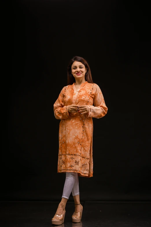 a woman in a tan dress stands on a black background