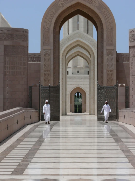two men wearing white are walking towards a massive archway