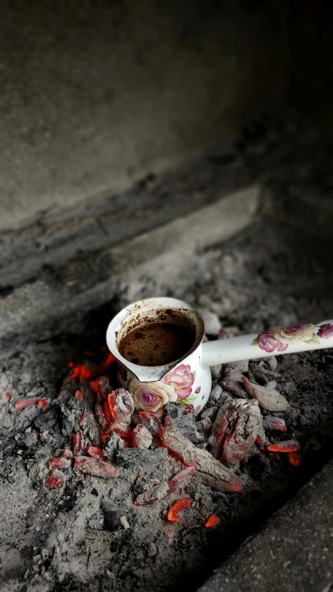 a cup of coffee sits on dirt and rocks