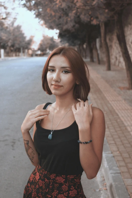 a woman poses next to a street, in front of trees