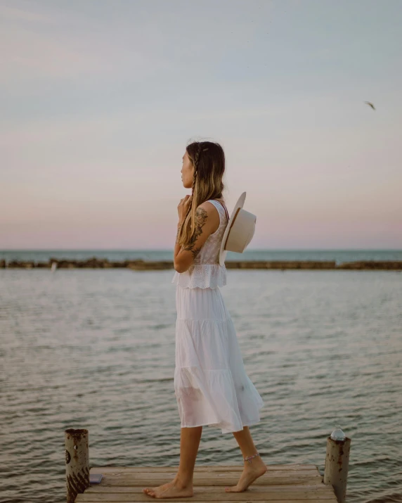 woman wearing white dress standing on a dock with hat