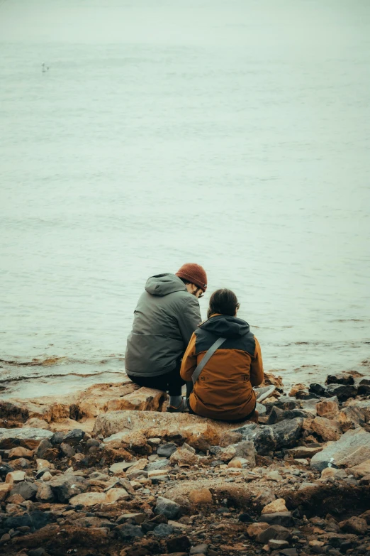 two people sitting on the rocks near water