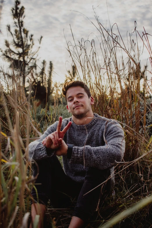 a man sitting in the middle of tall grass making the peace sign