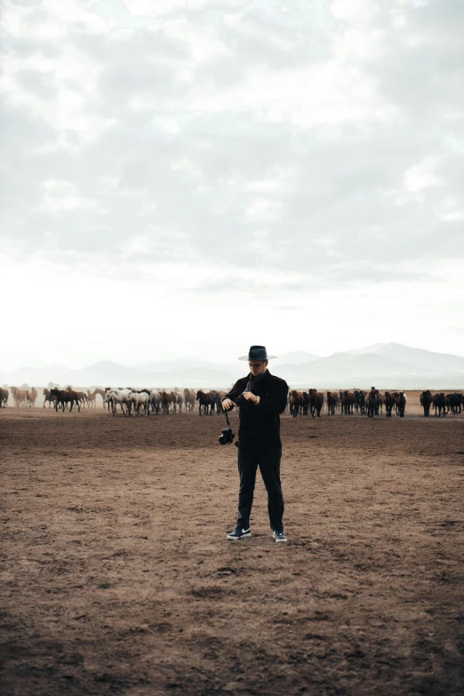 a man in a black jacket and hat is standing by a herd of cows