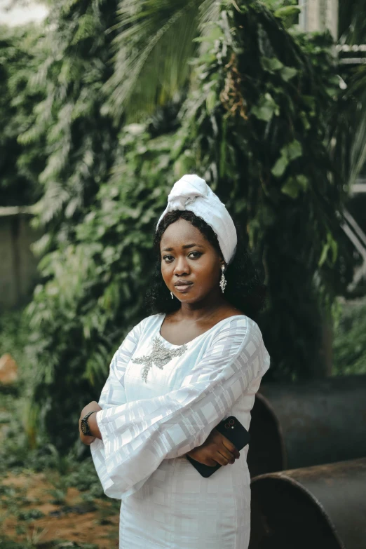 a woman wearing a headwrap standing next to green trees