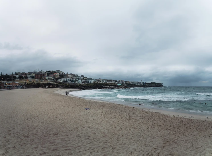 a sandy beach with houses on a hill in the distance