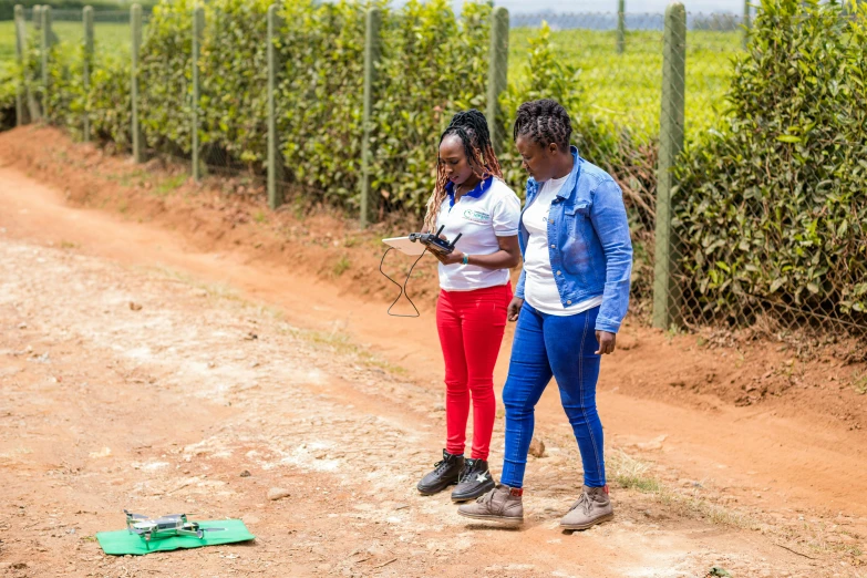 two women in blue and red clothes standing on a dirt road next to a wire fence